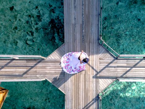 Romantic aerial shot of a couple embracing on a wooden boardwalk over clear turquoise water.