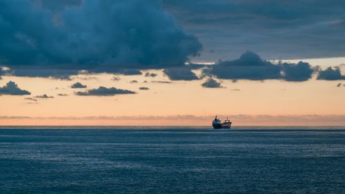 Free A cargo ship sails on the calm ocean under a cloudy sunset sky, creating a tranquil scene. Stock Photo
