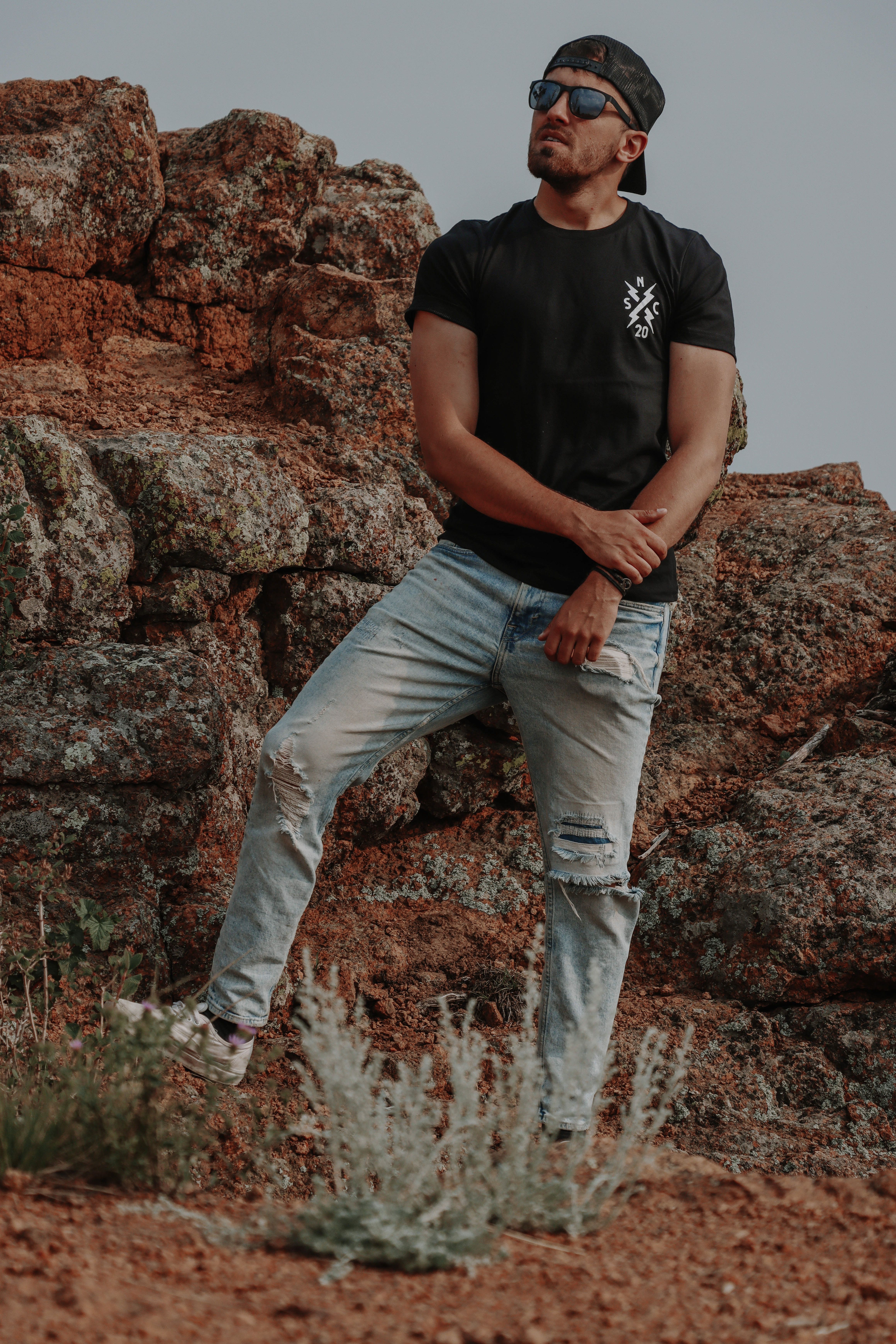 Man with sunglasses standing on rocky terrain in casual wear, outdoors.