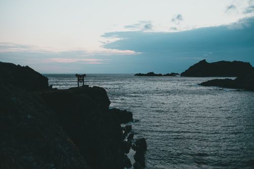 Free Beautiful coastal scene at dusk featuring rocky cliffs and calm sea under a moody sky. Stock Photo