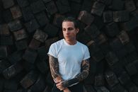 Adult man with tattoos posing with cobbled stones behind