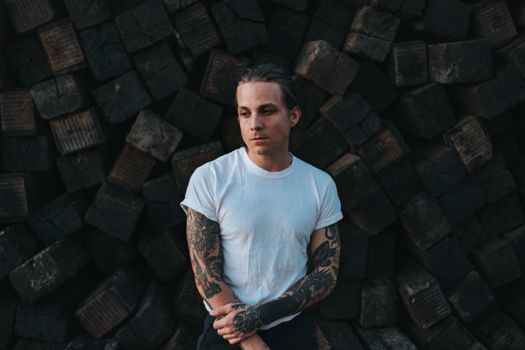 Adult man with tattoos posing with cobbled stones behind
