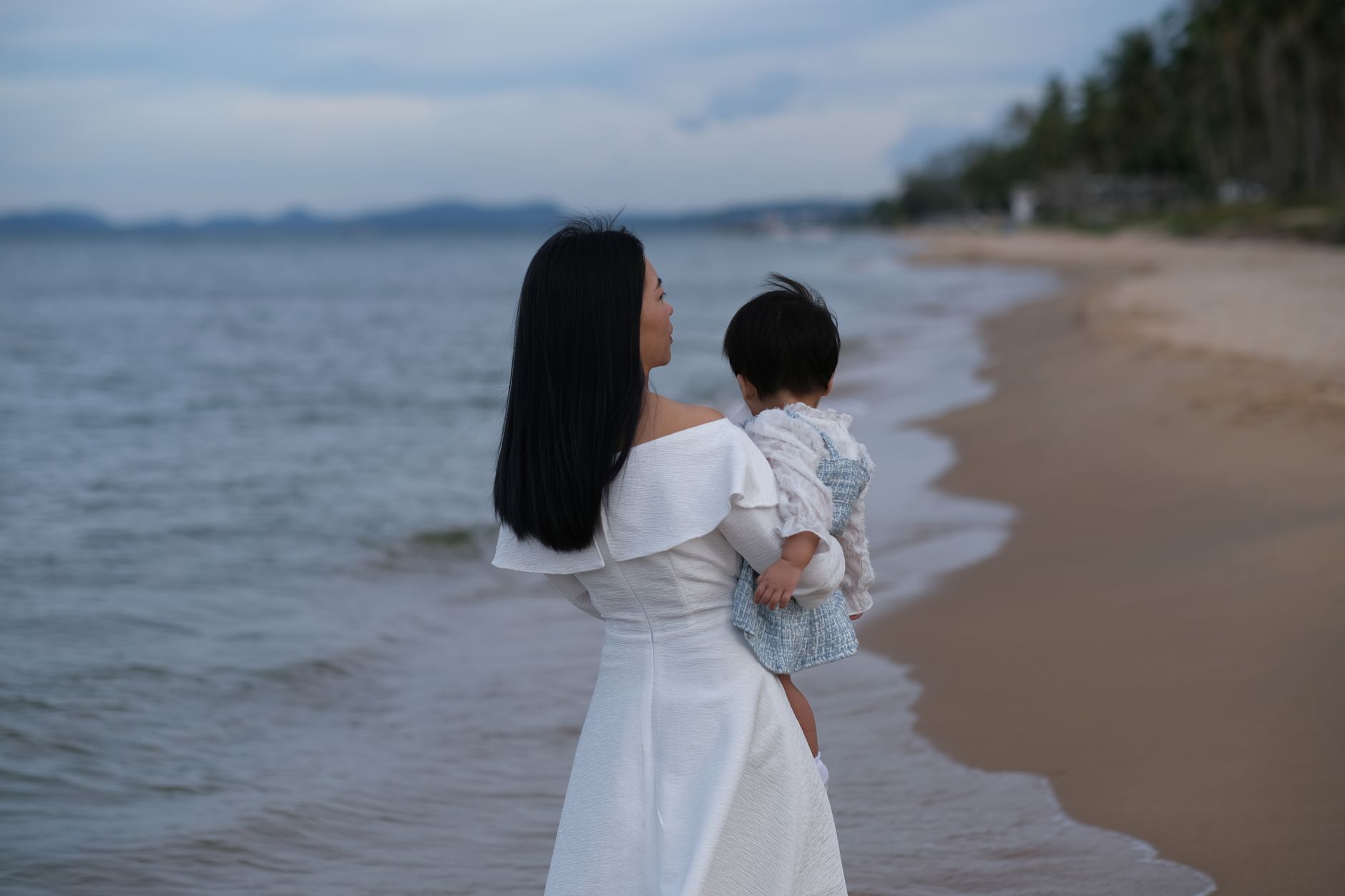 A mother holding her child walks along the serene beach of Phu Quoc, Vietnam at twilight.