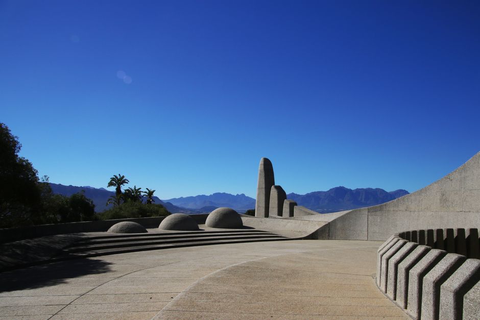 Modern stone structure with mountains and palm trees under a vivid blue sky.
