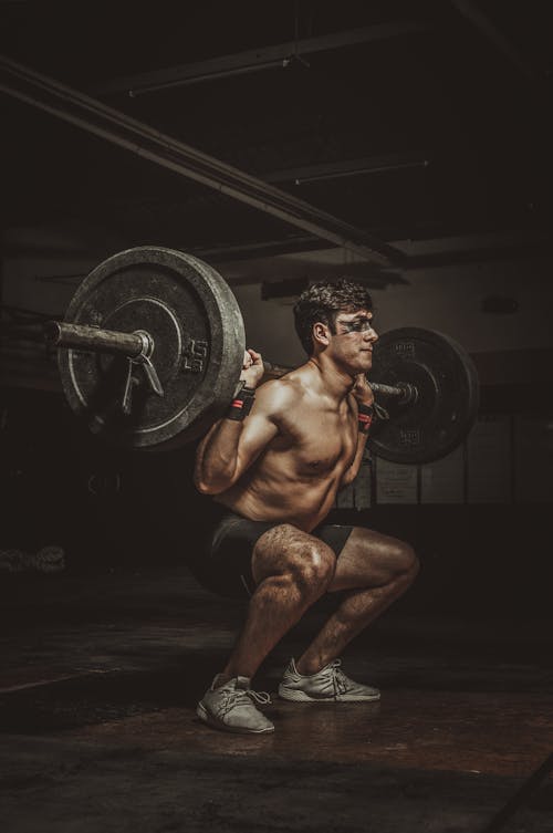 A Topless Man in Black Shorts Doing Squats with a  Barbell