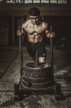 A shirtless man engages in a heavy sled push workout indoors, showcasing strength and endurance.