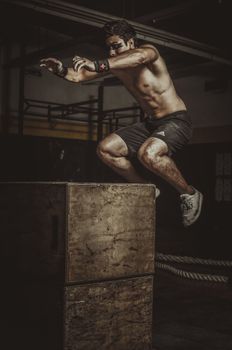 Shirtless man performing a high-intensity box jump exercise in a dimly lit gym.
