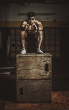 Shirtless man showcasing strength and balance during box jump workout with wooden boxes, indoors.