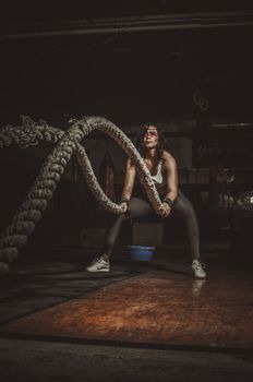 Woman performing an intense battle rope exercise in a dimly lit gym, showcasing strength and dedication.