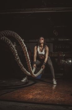 Woman engaging in an intense battle ropes workout in a gym setting for fitness.