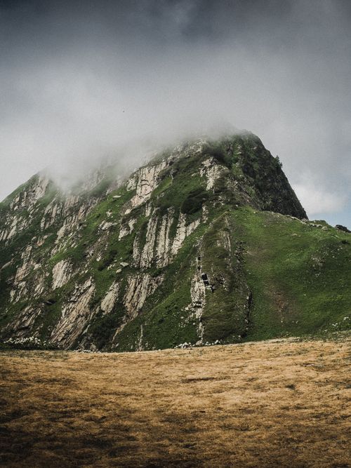 Free Scenic view of a lush green mountain partially covered in mist under a cloudy sky. Stock Photo