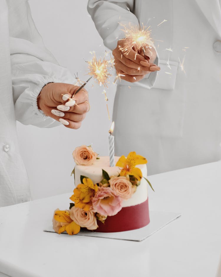 Cake On White Table Beside People Holding Sparklers