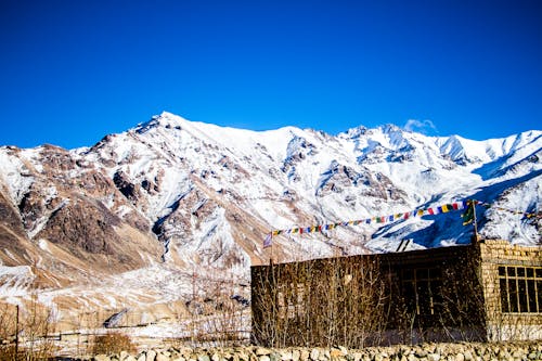 Stone Building at the Base of Snow-covered Mountain Range Under Clear Bright Blue Sky