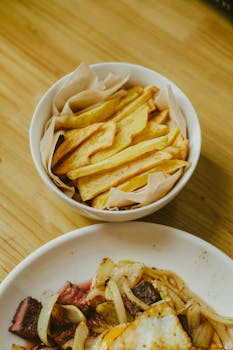 Crispy homemade french fries served in a bowl on a wooden table, perfect for a tasty snack.