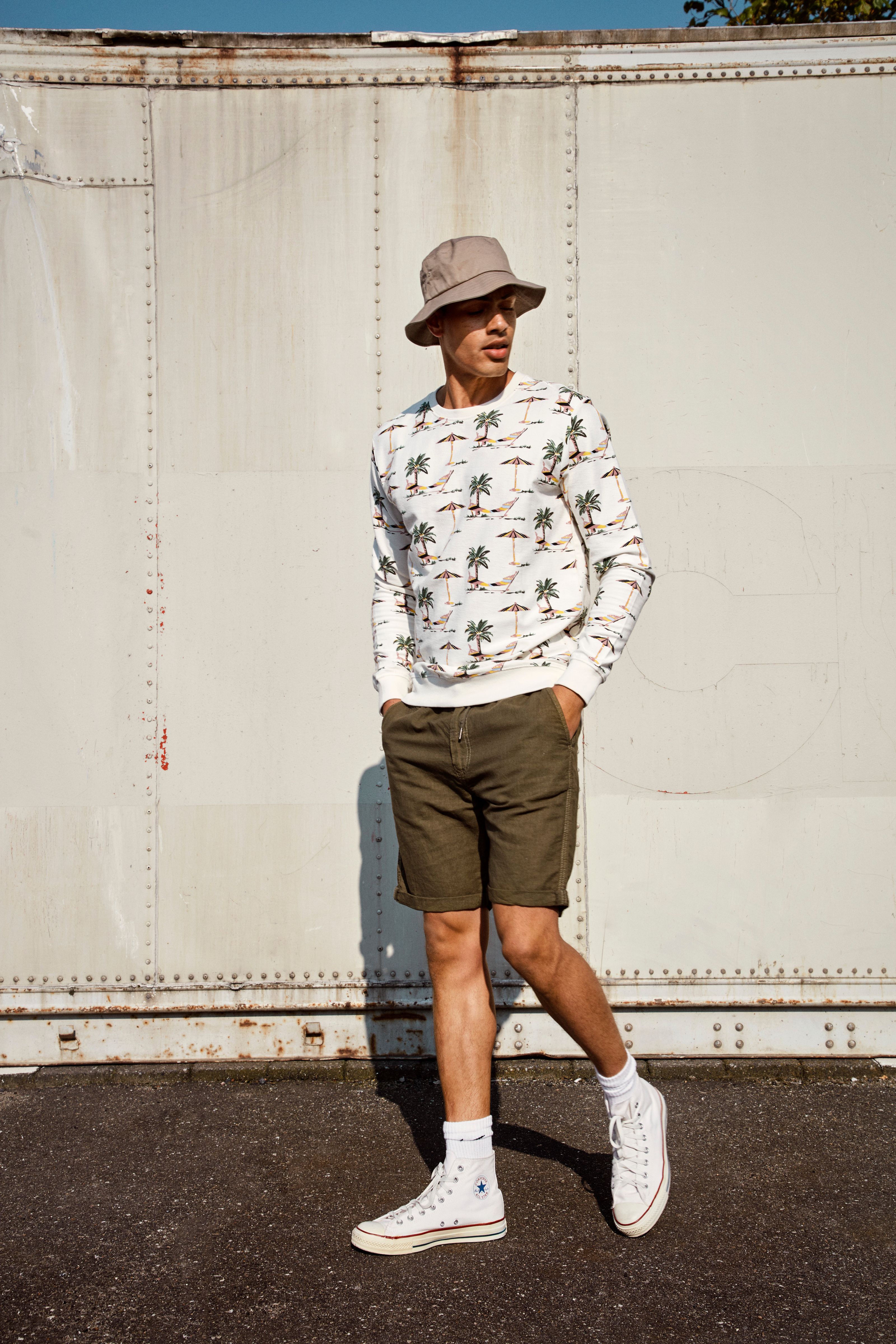 Homem estiloso em um traje casual de verão com chapéu estilo balde em um ambiente urbano ao ar livre.