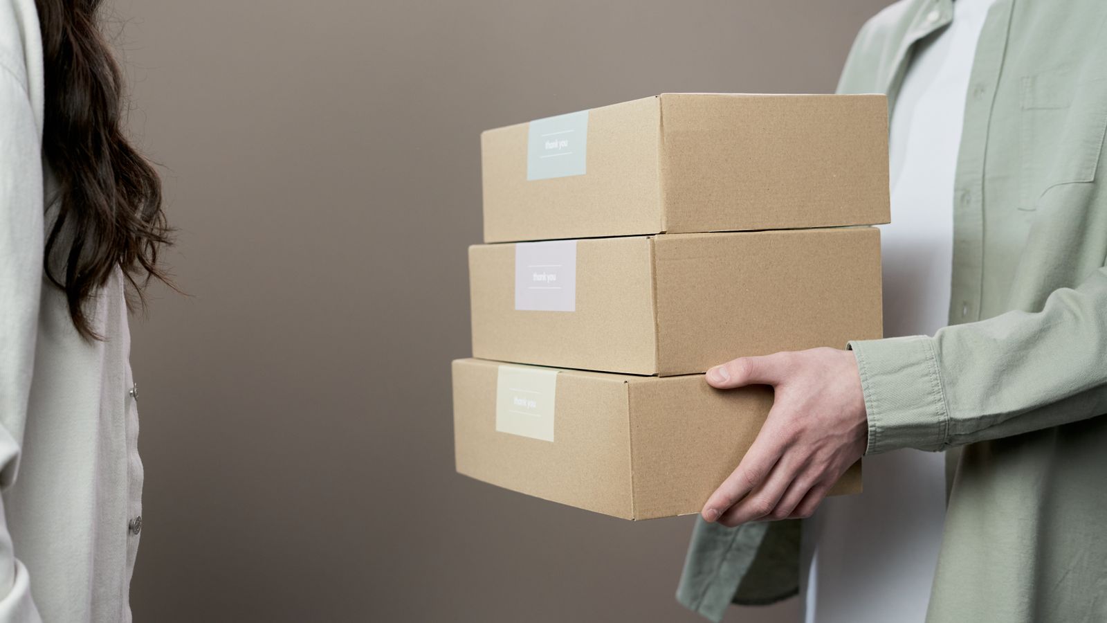 Two people exchanging stacked cardboard boxes against a neutral gray background in a studio setting.