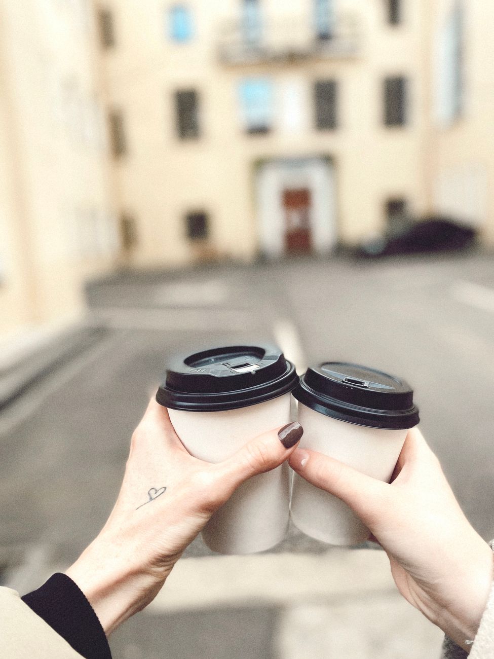 Close-up of two hands holding coffee cups with lids. Urban background.. close, hands, holding