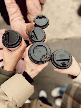 Top view of five people holding disposable coffee cups outdoors, showcasing friendship and warmth.