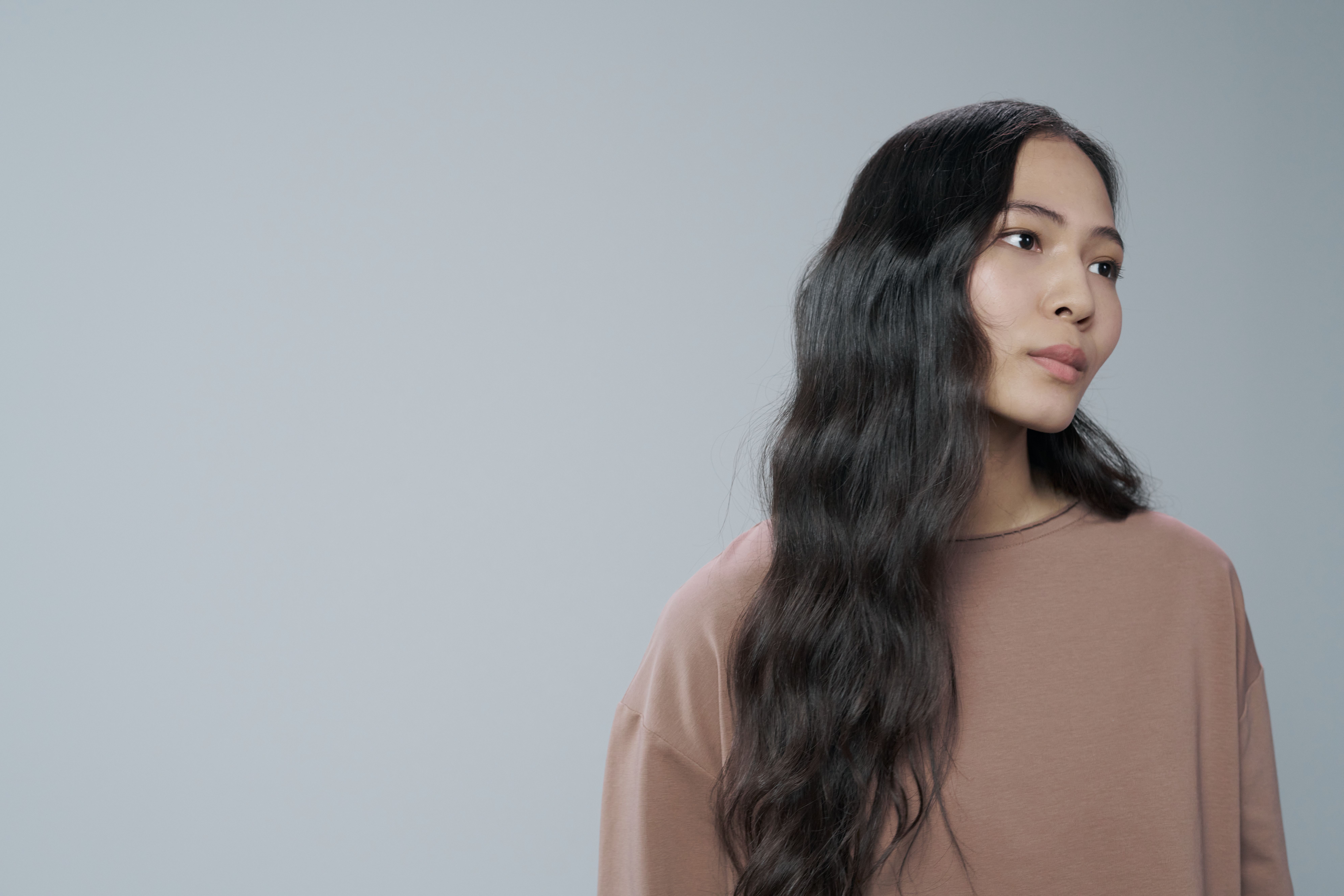 Portrait of an Asian woman in a brown shirt looking away, with a gray backdrop.
