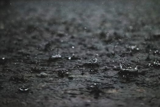 Close-up of raindrops hitting a pavement, creating ripples and splashes.