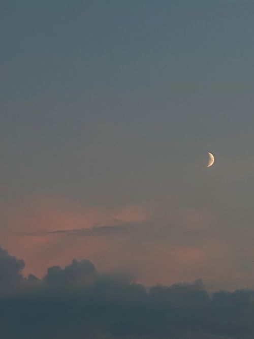 Free A serene image of a crescent moon in a colorful evening sky with clouds. Stock Photo