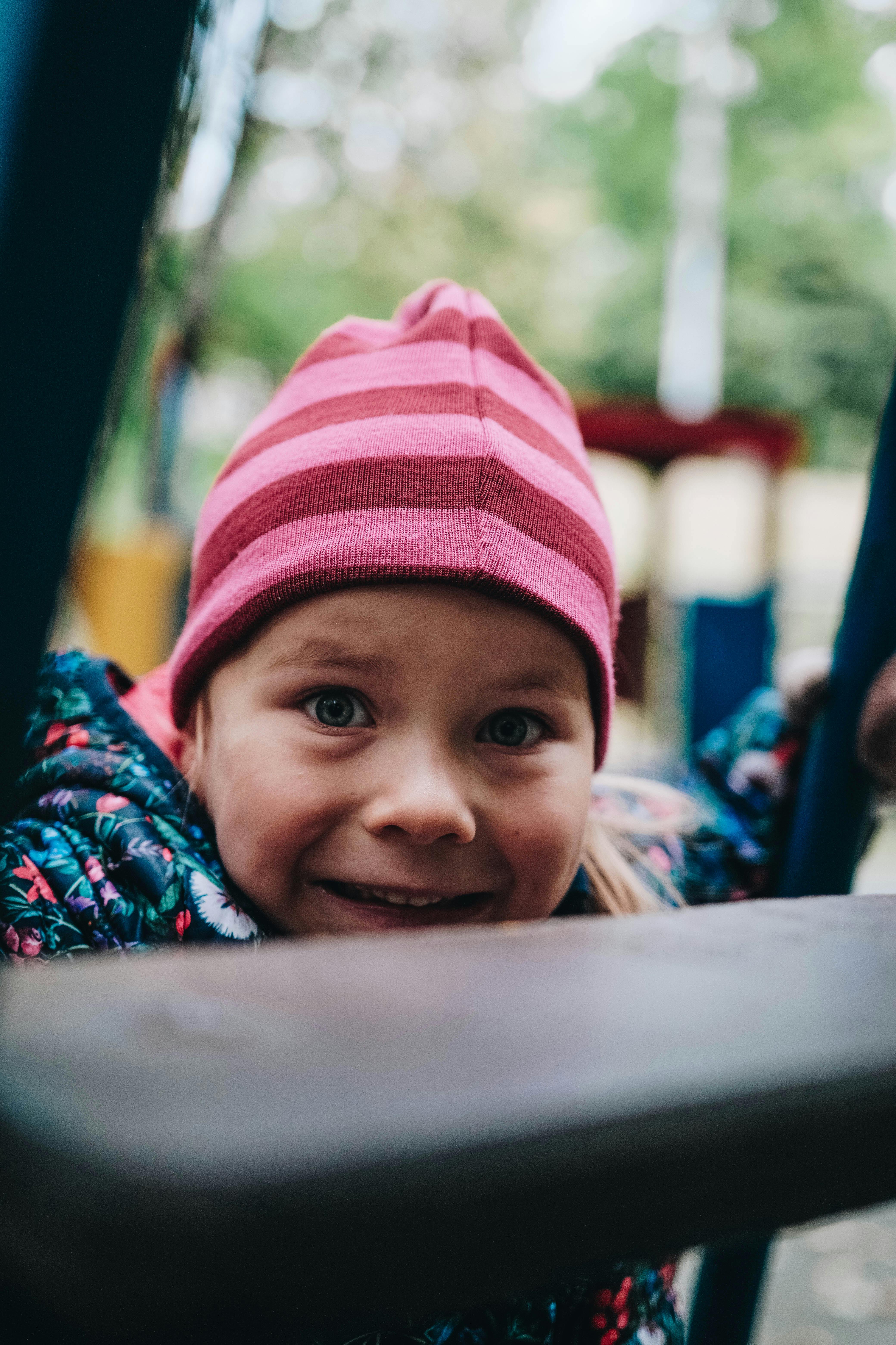 A joyful child wearing a pink beanie enjoys a playful moment at an outdoor playground.