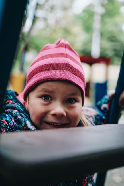 A joyful child wearing a pink beanie enjoys a playful moment at an outdoor playground.