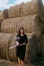 Photo of a Woman in a Black Dress Standing Near Hay Bales