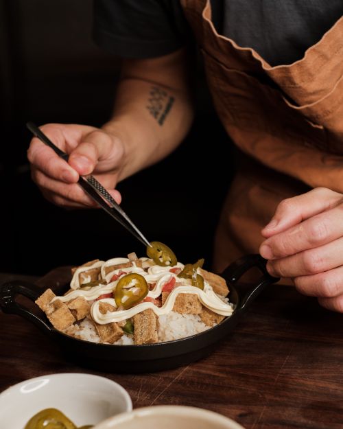 Free Close-up of a chef delicately plating a dish of tofu sisig garnished with jalapeno slices and mayonnaise. Stock Photo