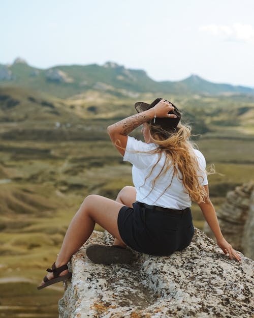 Woman in White Shirt and Black Shorts Sitting on Rock