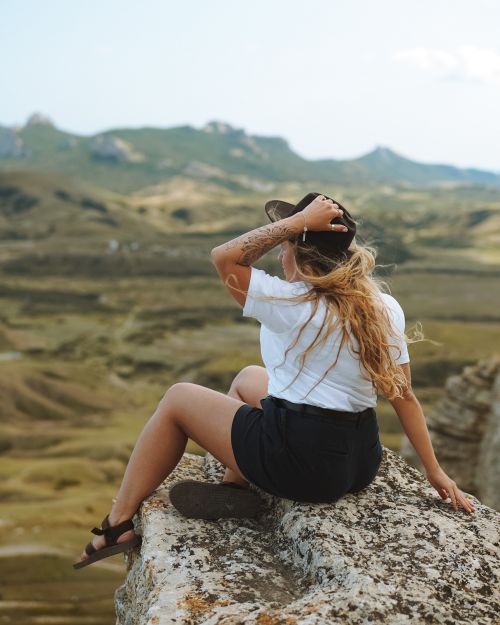 Free Young woman sitting on a cliff, enjoying the vast mountain landscape and serenity. Stock Photo
