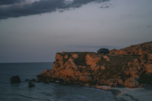Free A scenic view of a rugged coastal cliff during twilight with a car parked on top. Stock Photo