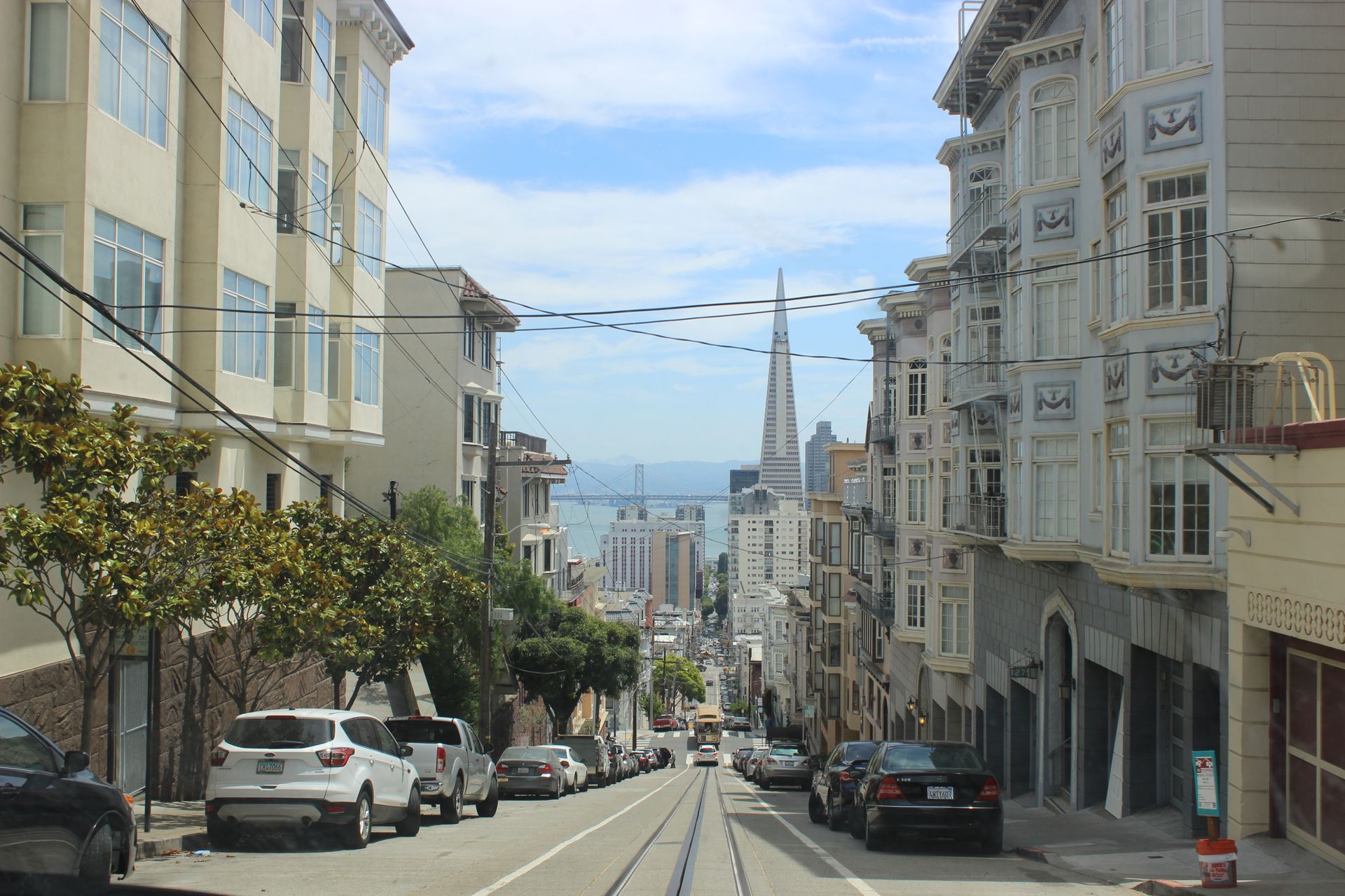 A San Francisco hill street with cable car tracks, looking down toward the Transamerica Pyramid