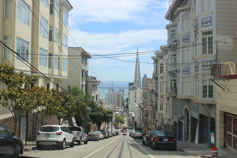 A San Francisco hill street with cable car tracks, looking down toward the Transamerica Pyramid