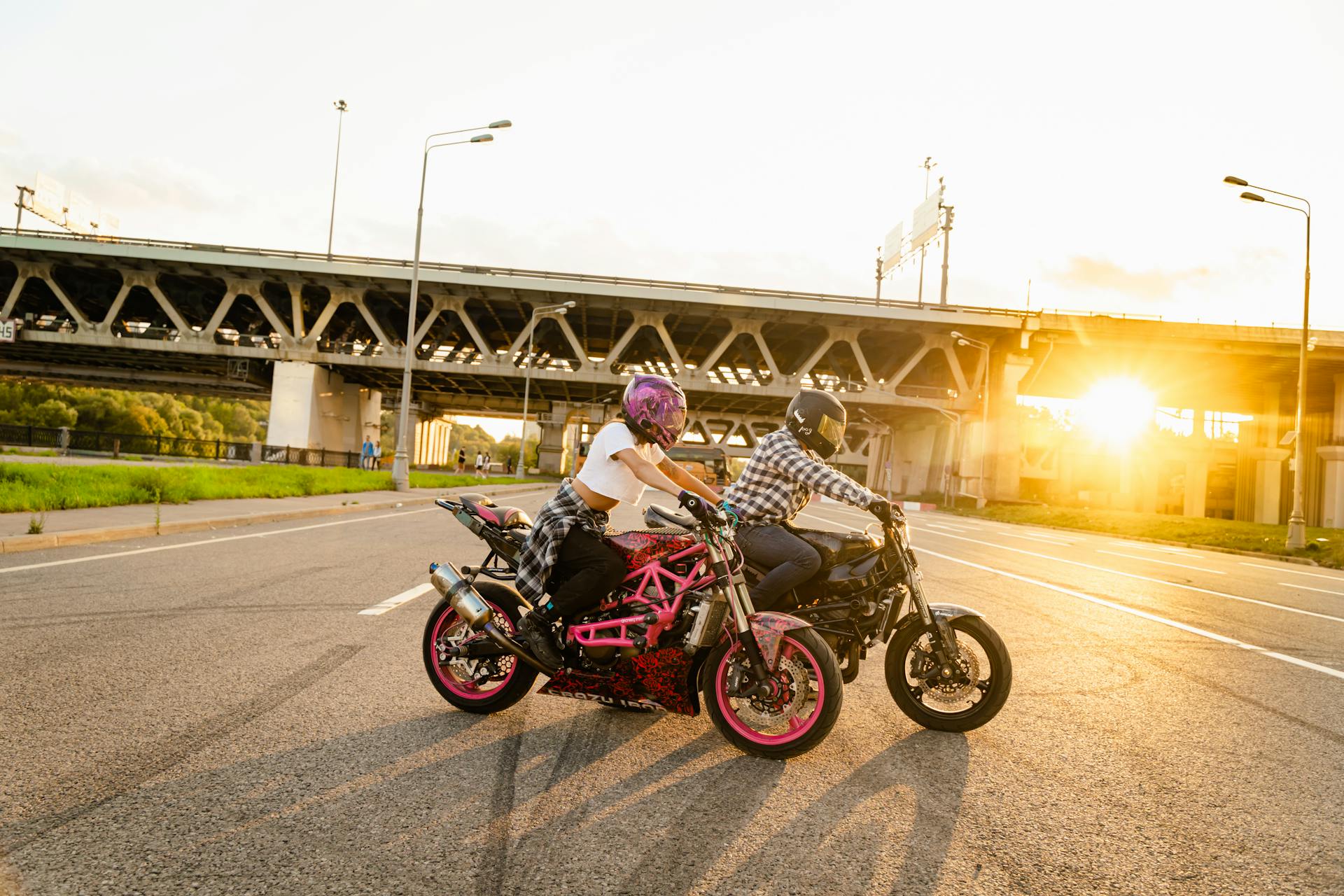 Two bikers riding motorcycles under a bridge during sunset, capturing adventure and freedom.