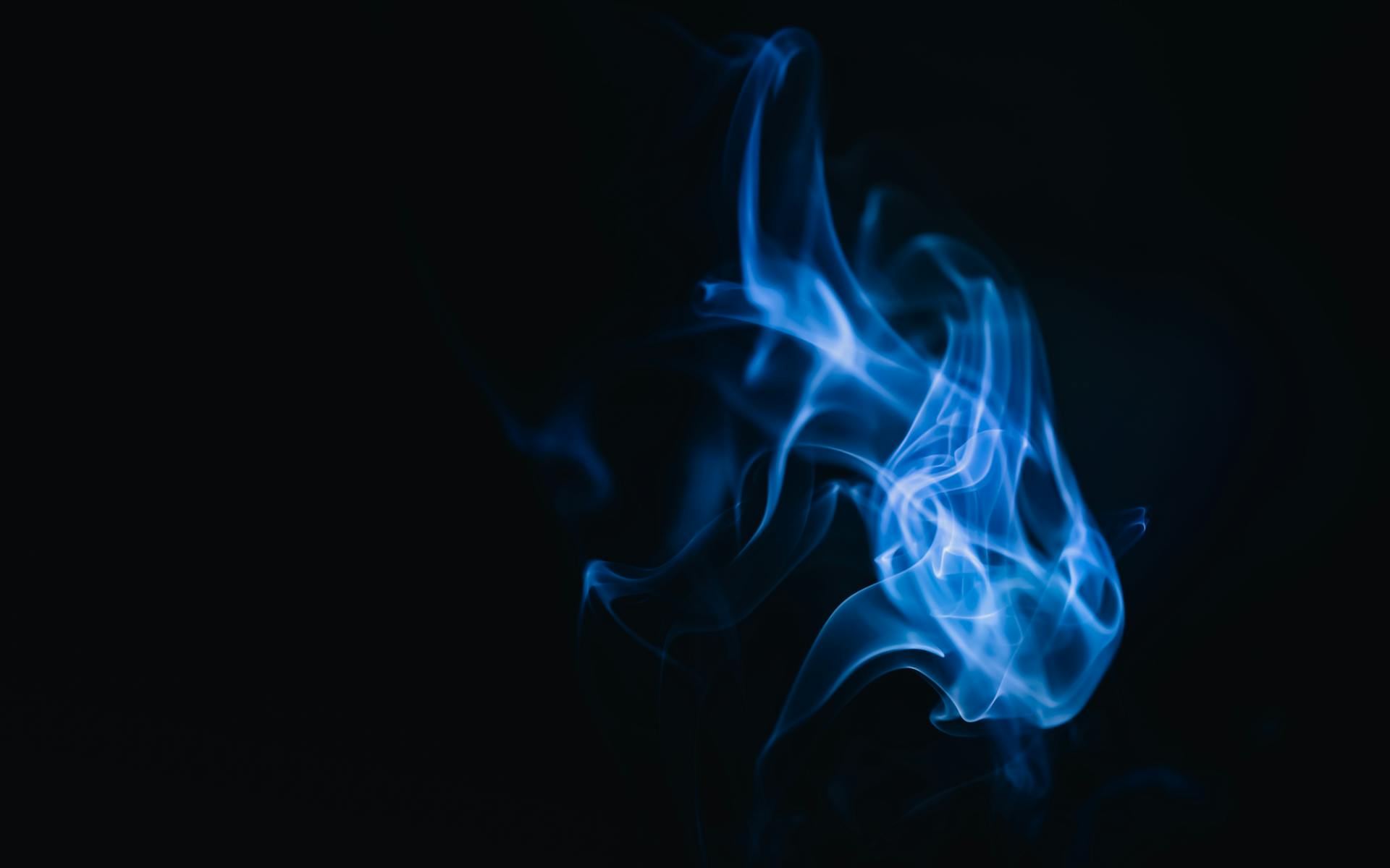 Blue smoke swirls creating abstract forms on a dark background, evoking a mysterious and dreamy atmosphere.