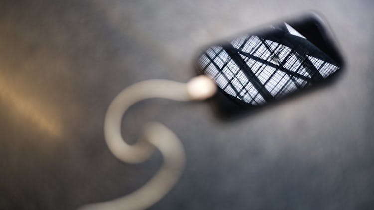 A Charging Cellphone On Gray Surface With A Steel Fence Reflection On Srcreen