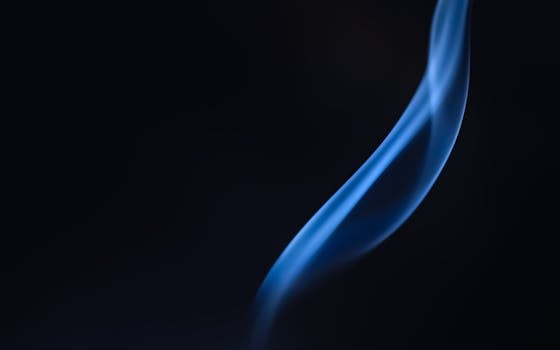 A graceful swirl of blue smoke on a dark backdrop creates a mysterious, abstract art piece.