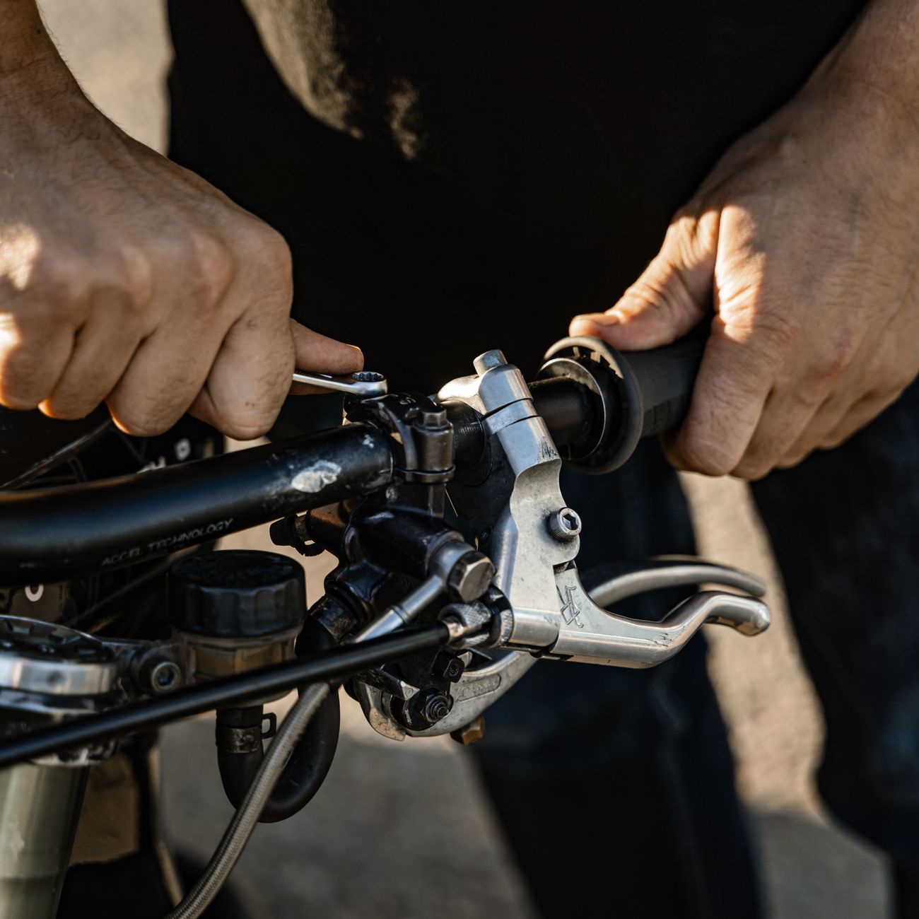 Close-up of a person repairing motorcycle handlebars outdoors in sunlight.