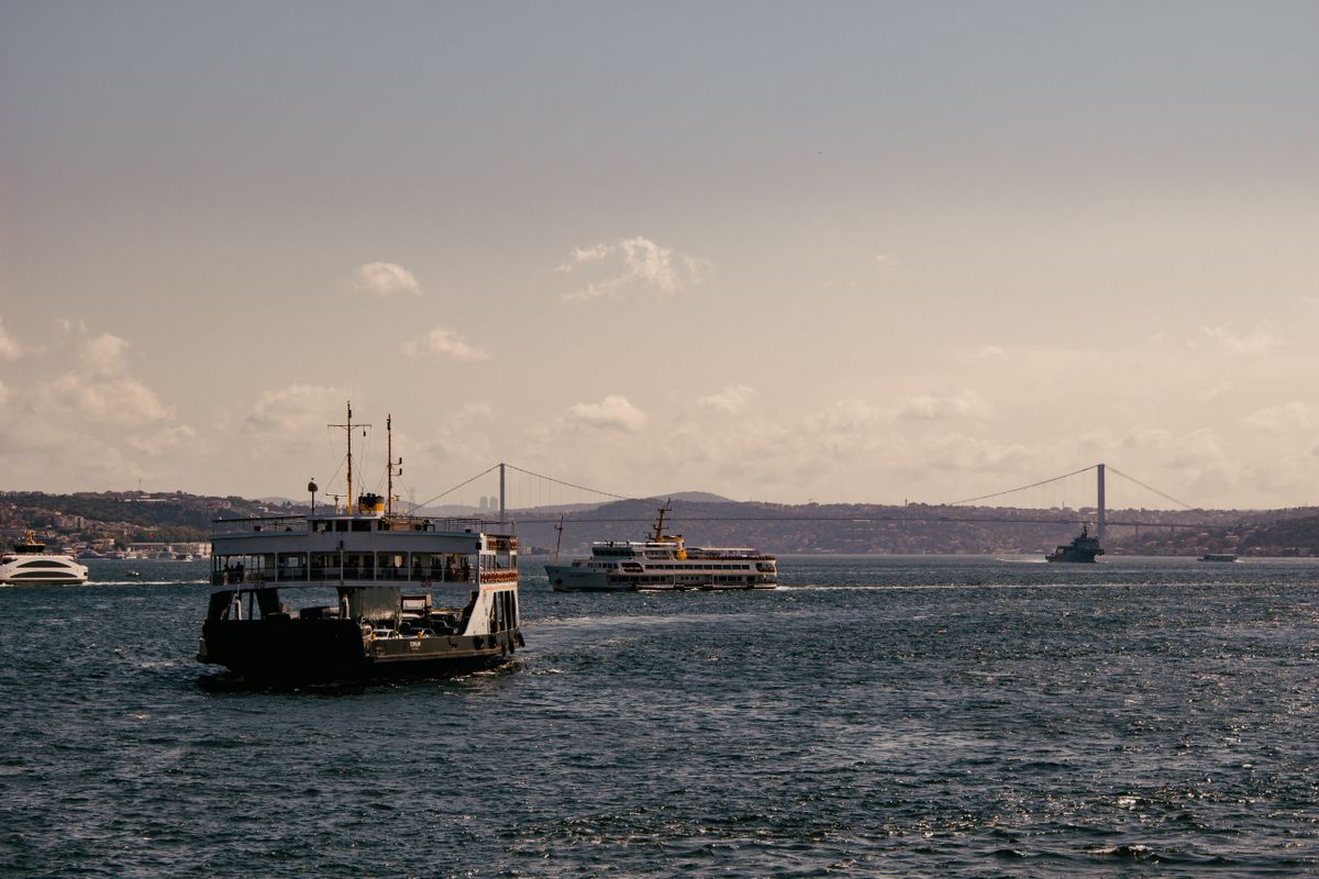 Two passenger ferries crossing paths on the Bosphorus with the suspension bridge visible in the distance