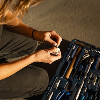 A person in sunlight handling tools from a blue toolbox, viewed from above.