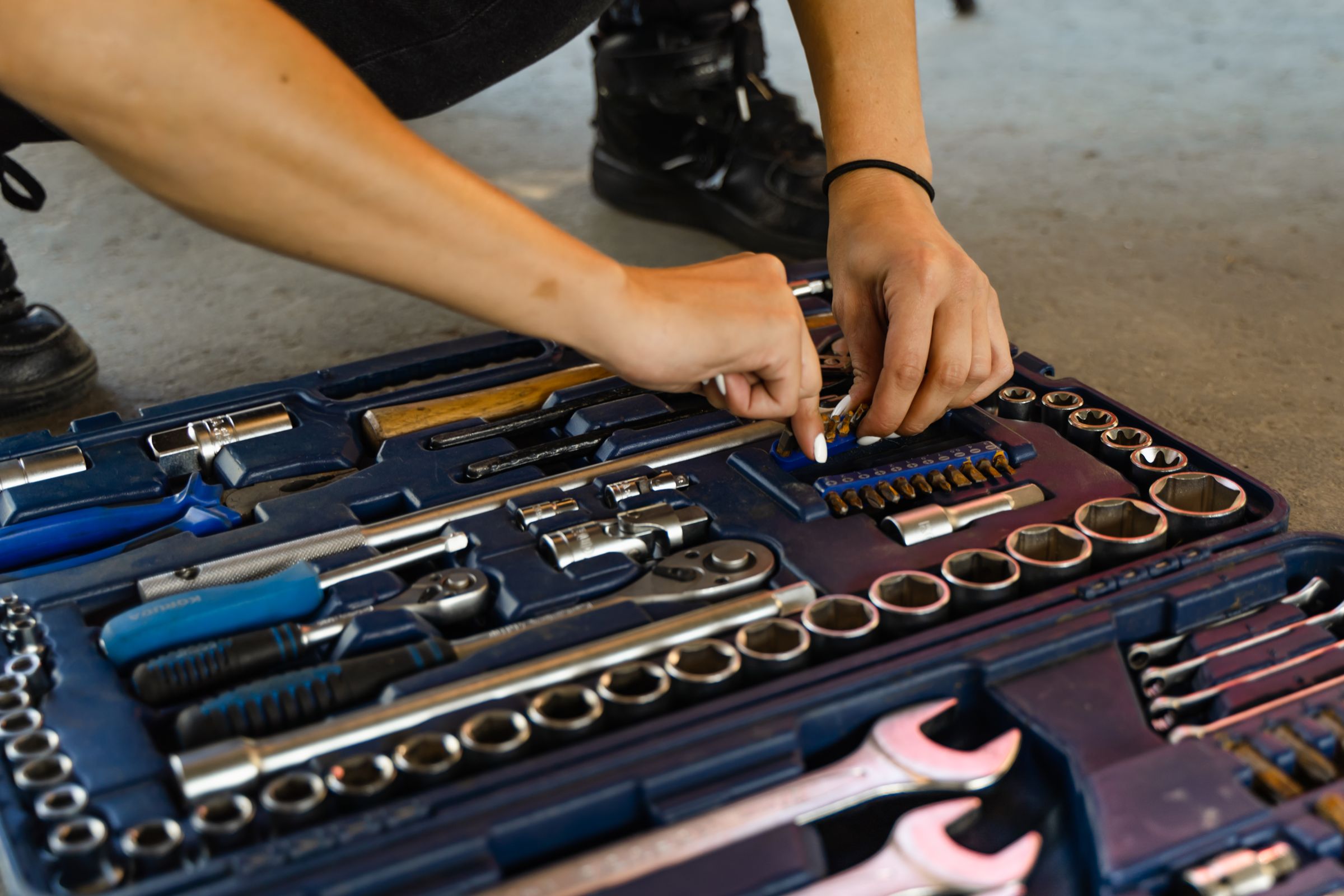 Hands selecting a ratchet from an organized toolbox containing sockets, screwdrivers, and repair tools
