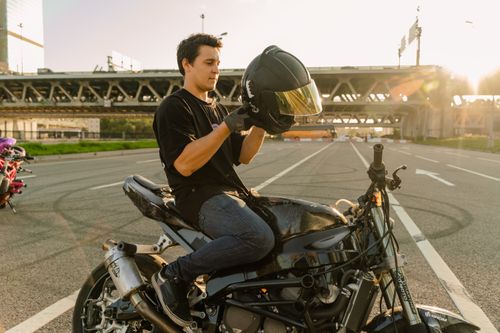 Free A man sitting on a motorcycle, putting on a helmet, on a city road at sunset. Stock Photo