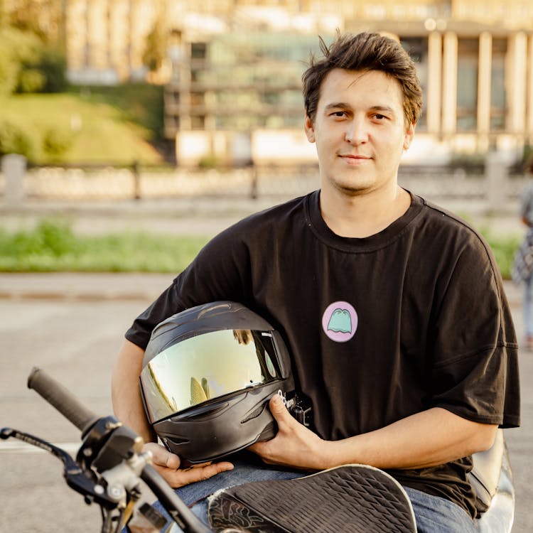 A Man Sitting On A Parked Motorcycle Holding A Black Helmet