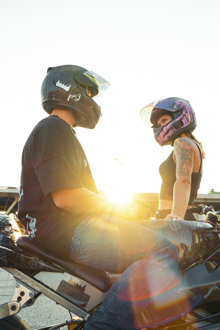 Man And Woman Wearing Helmet Sitting On Motorcycle While Looking At Each Other 