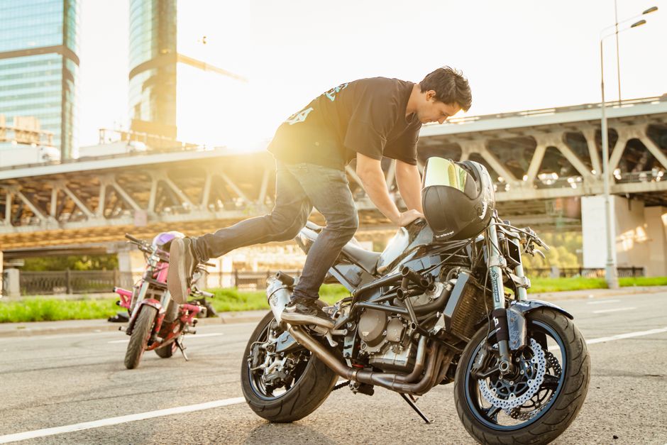 A motorcyclist executes a daring stunt in an urban street setting with sunlight in the background.