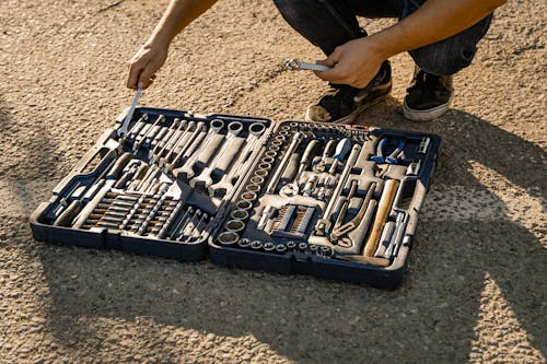 Person Crouching Near a Set of Hand Tools and Wrenches on Ground