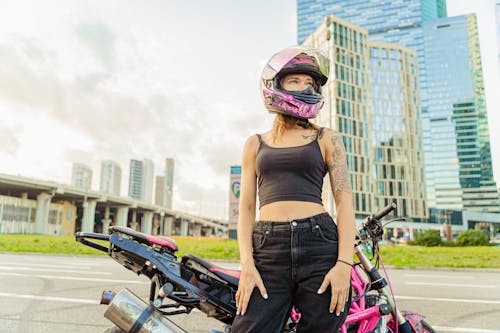 Woman in Black Spaghetti Strap Crop Top Standing Beside a Pink Motorcycle Wearing Safety Helmet