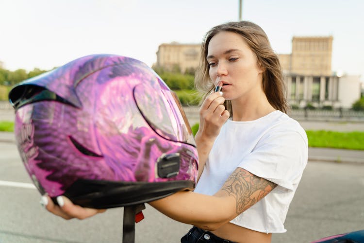 Woman Holding Helmet While Applying Lipstick