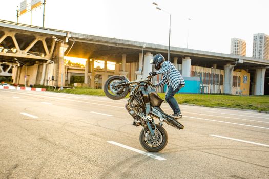 Motorcyclist performing a thrilling stunt on an empty city road near urban bridges.